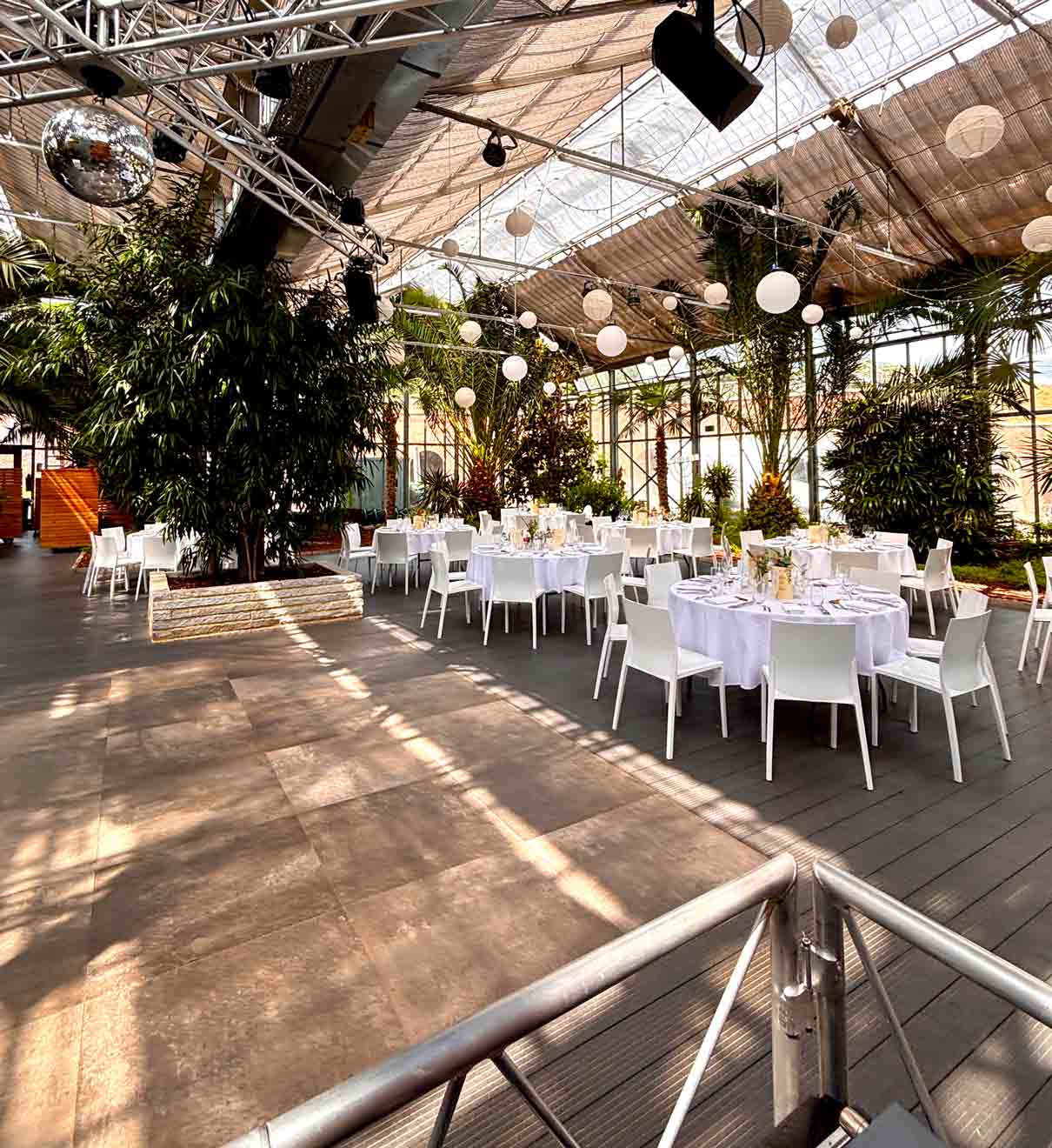 Blumenhalle Jülich – Hochzeitslocation mit Tanzfläche und mediterranem Ambiente Blick in die festlich dekorierte Blumenhalle Jülich mit runder Tanzfläche, gedeckten Tischen und mediterranen Pflanzen<br />